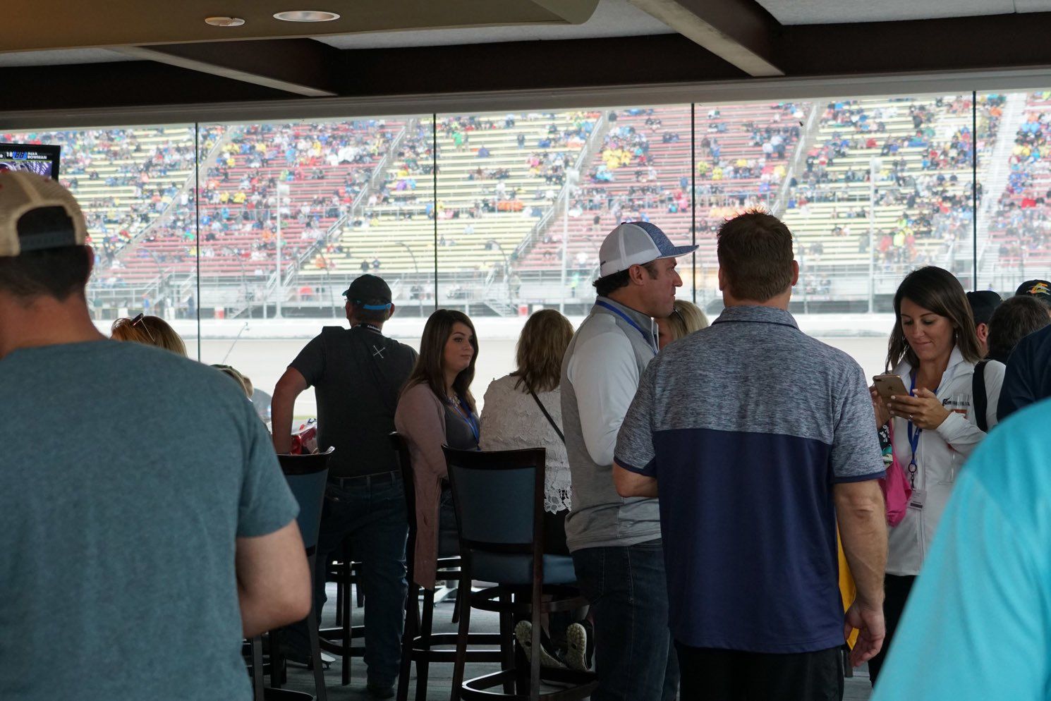 A group of people are standing in a room with a view of a race track.