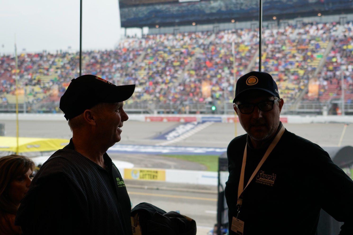 Two men are standing in front of a window at a race track talking to each other.