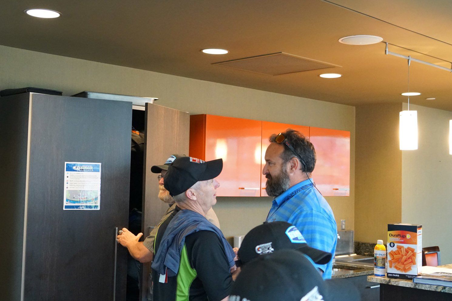A group of men are standing in a kitchen talking to each other