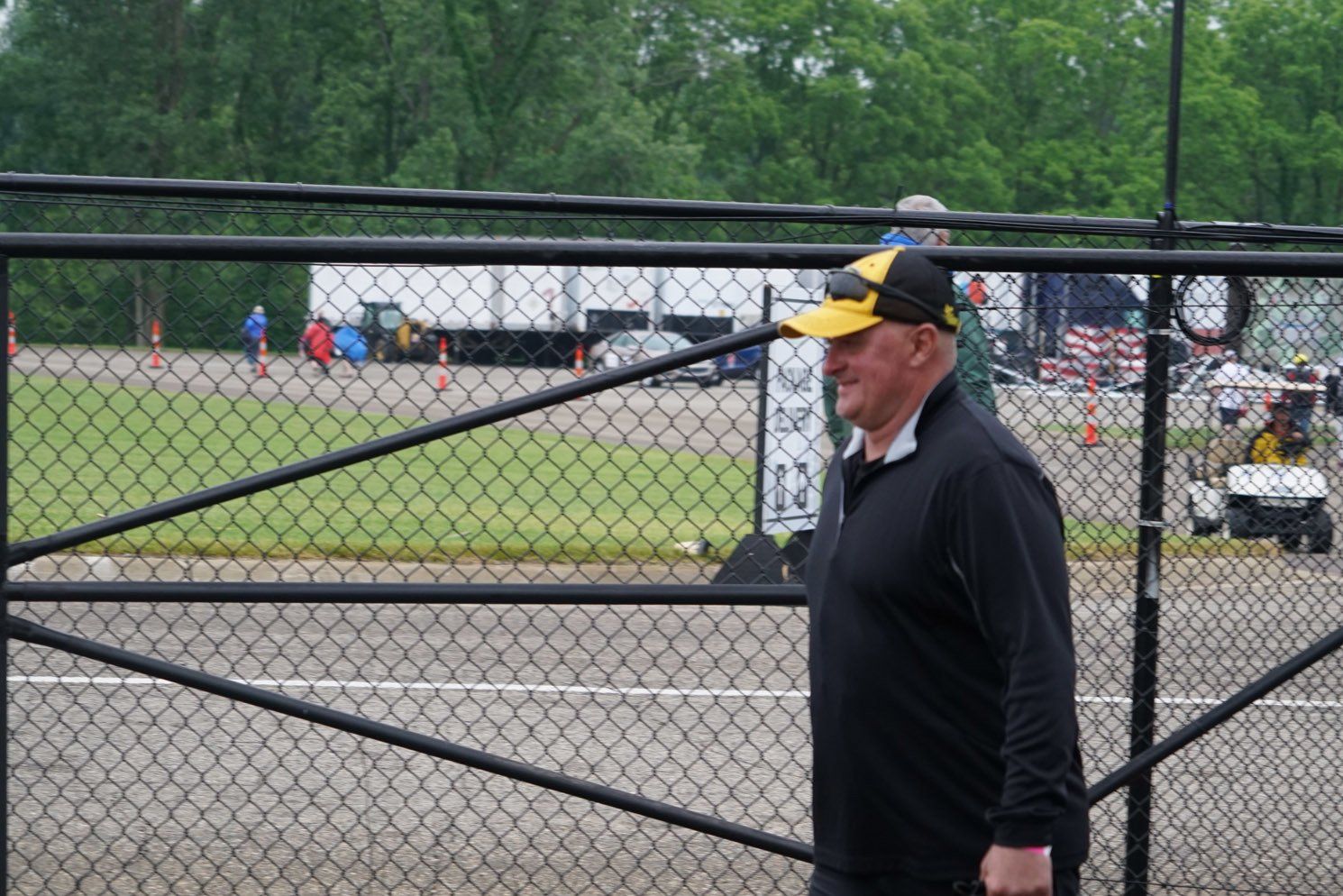 A man wearing a yellow hat is walking through a chain link fence