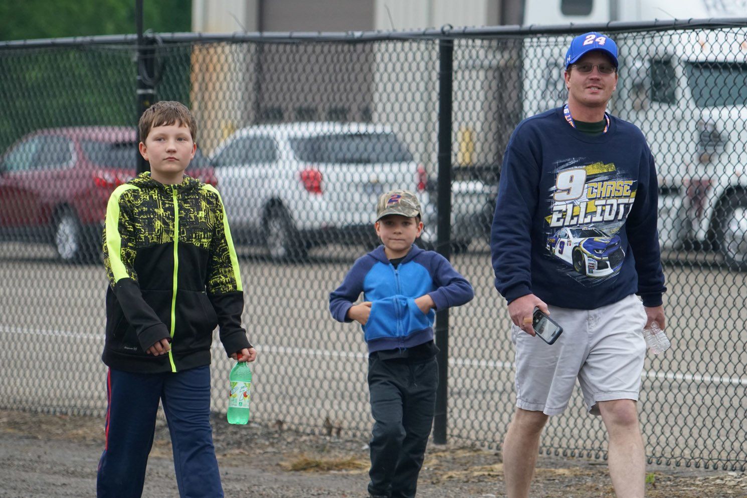 A man and two boys are walking in front of a chain link fence.