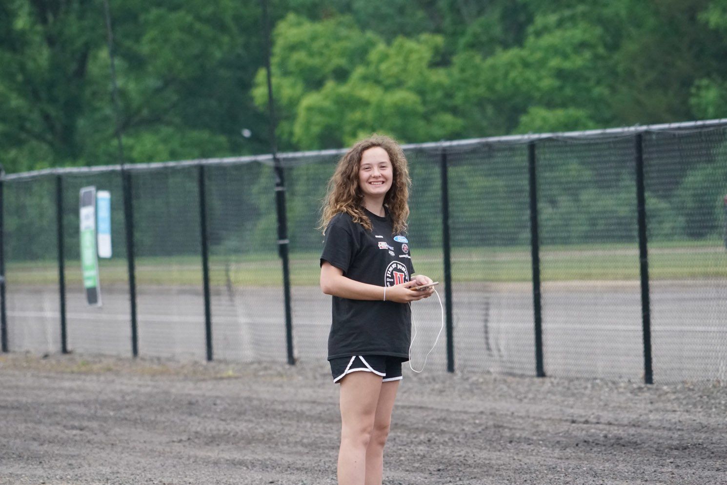 A young girl is standing in front of a fence in a field.