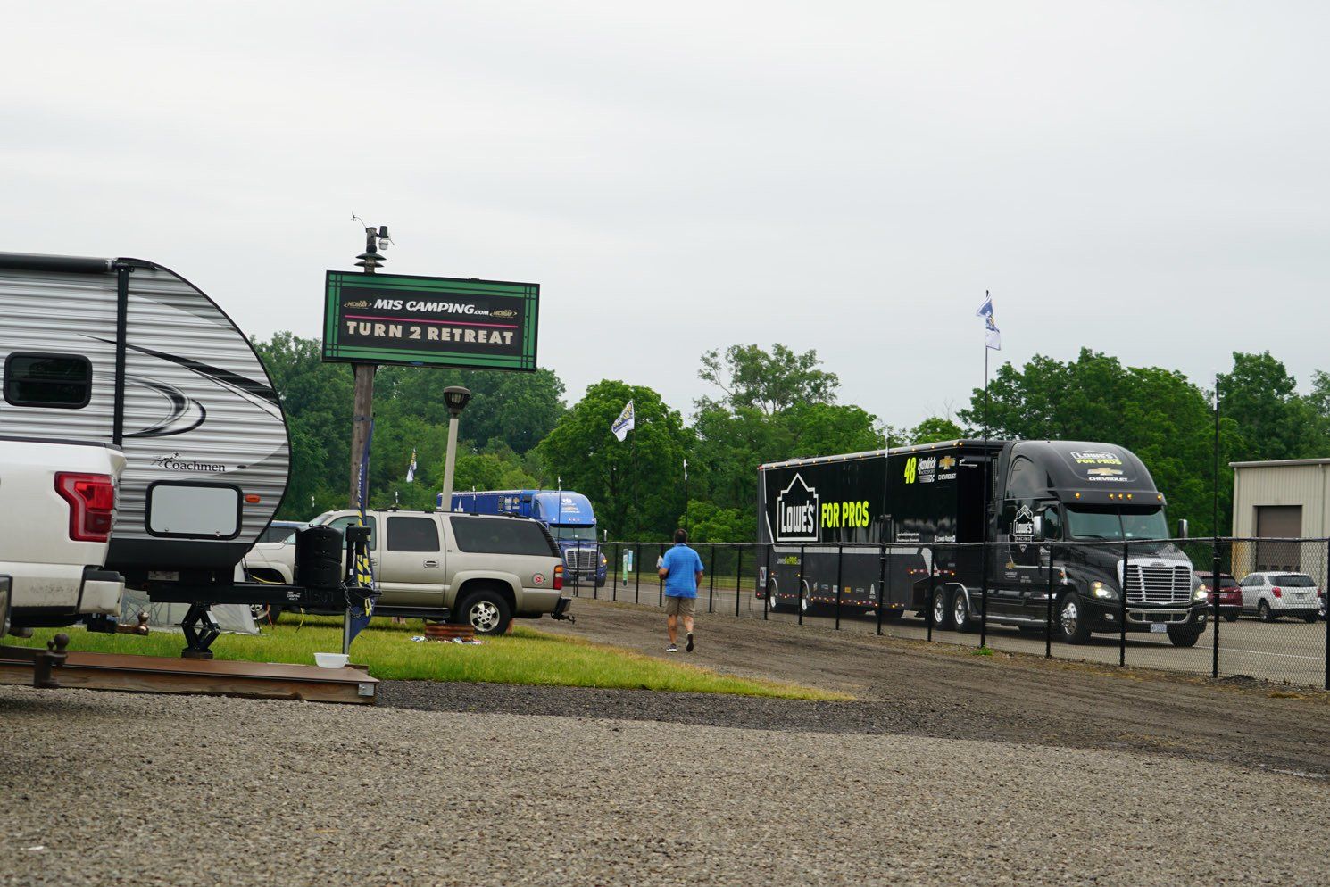 A rv is parked in a gravel lot next to a truck.
