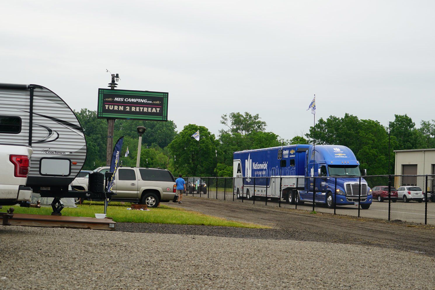 A lot of trucks and trailers are parked in a gravel lot.