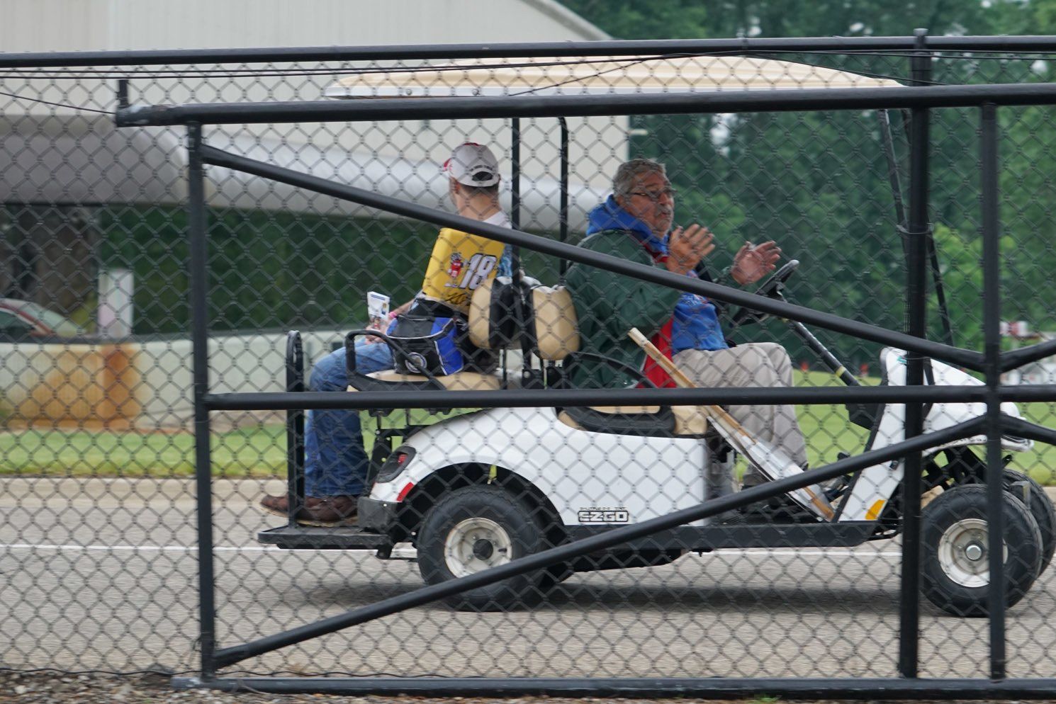 Two men are riding a golf cart through a chain link fence.