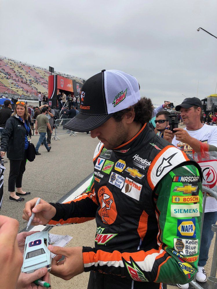 A race car driver is signing autographs for fans at a race track.
