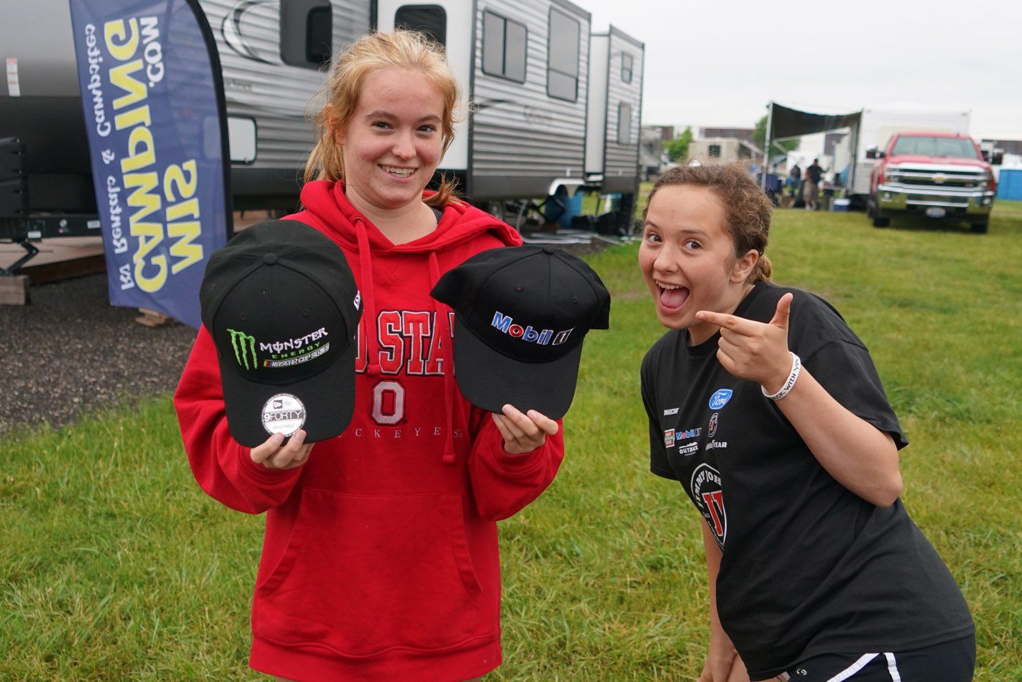 Two girls holding hats in front of a banner that says camping