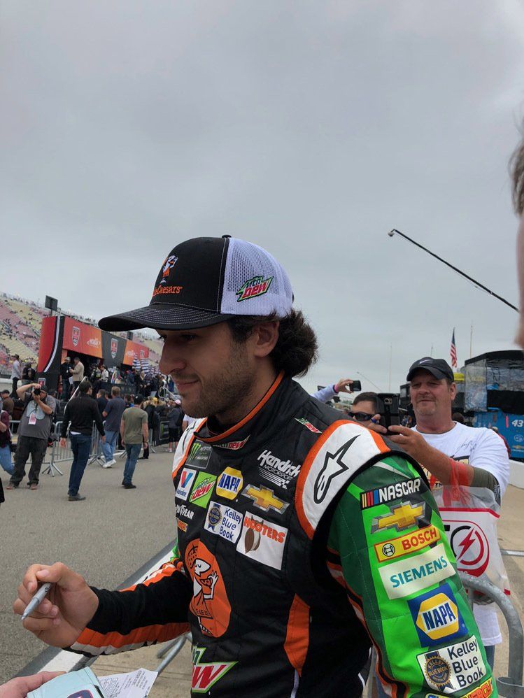 A race car driver is signing autographs for fans at a race track.