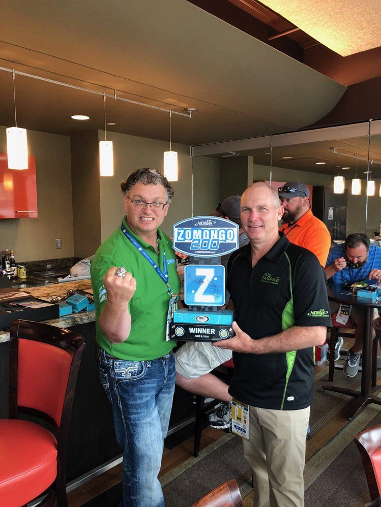 Two men are standing next to each other in a restaurant holding a trophy.