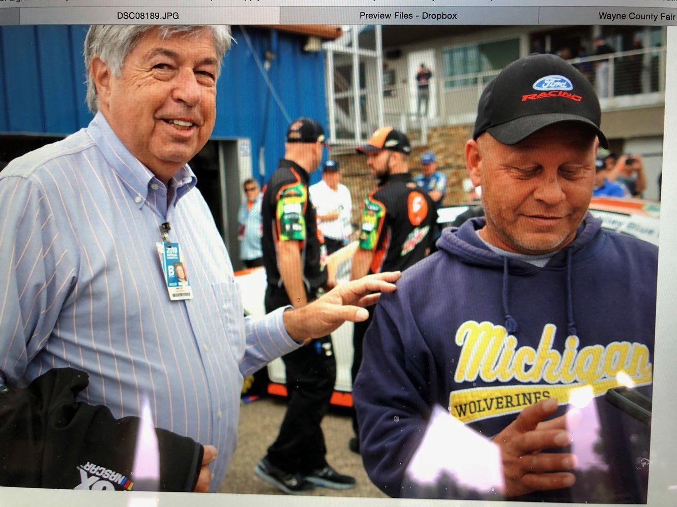 A man wearing a michigan wolverines sweatshirt stands next to another man