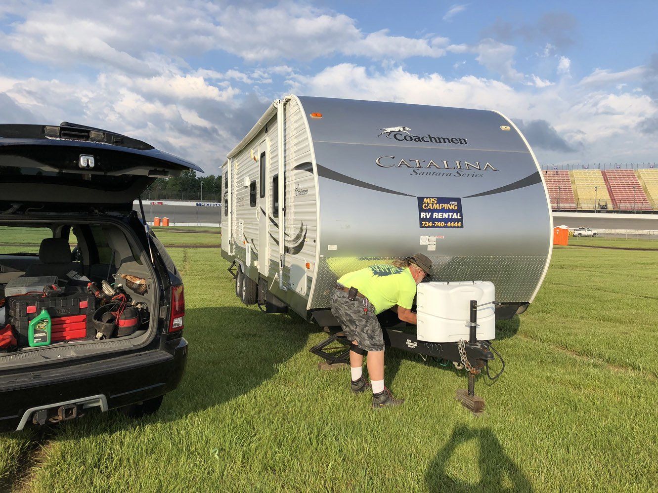 A man is working on a trailer in a field next to a car.