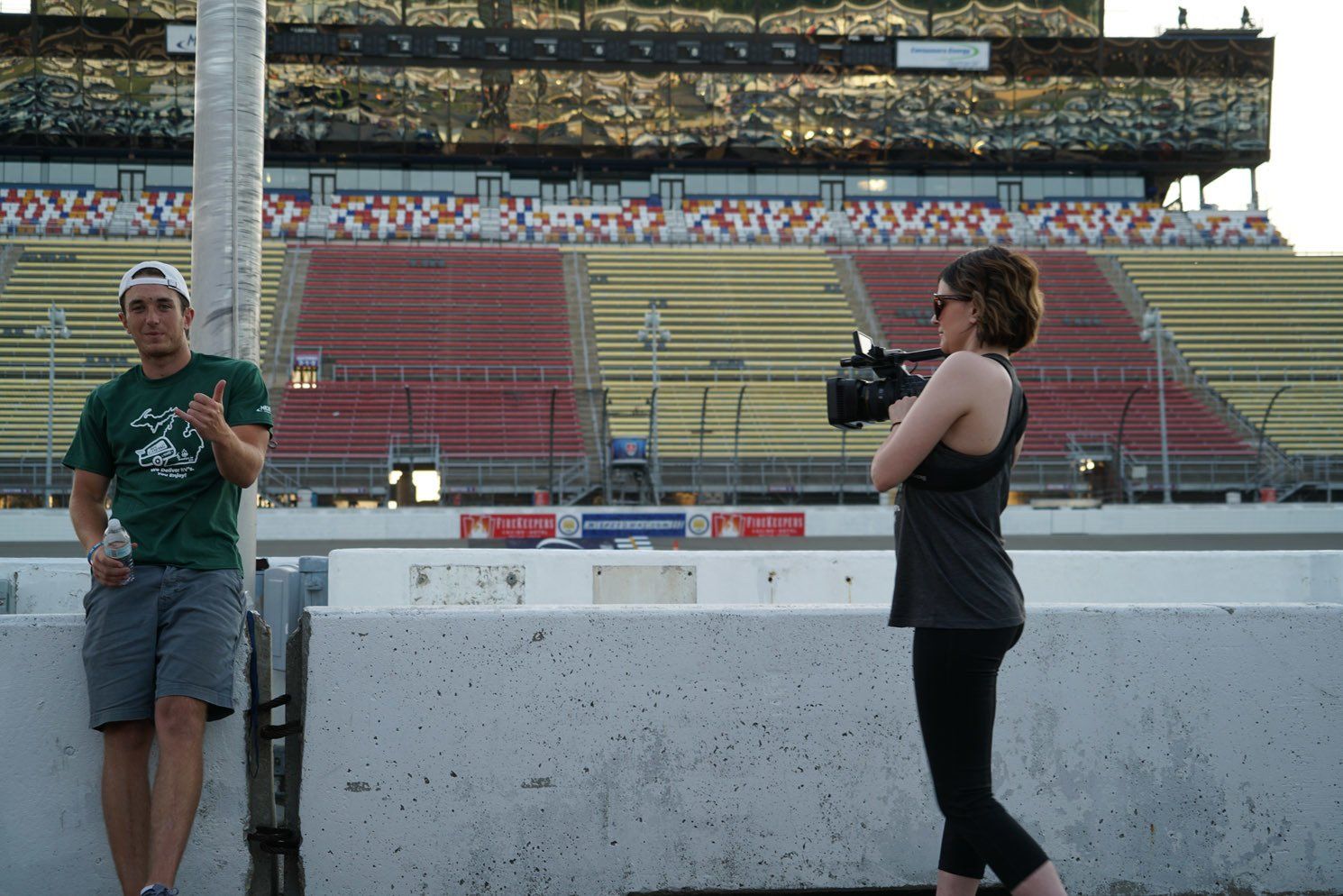 A man in a green shirt stands next to a woman holding a camera