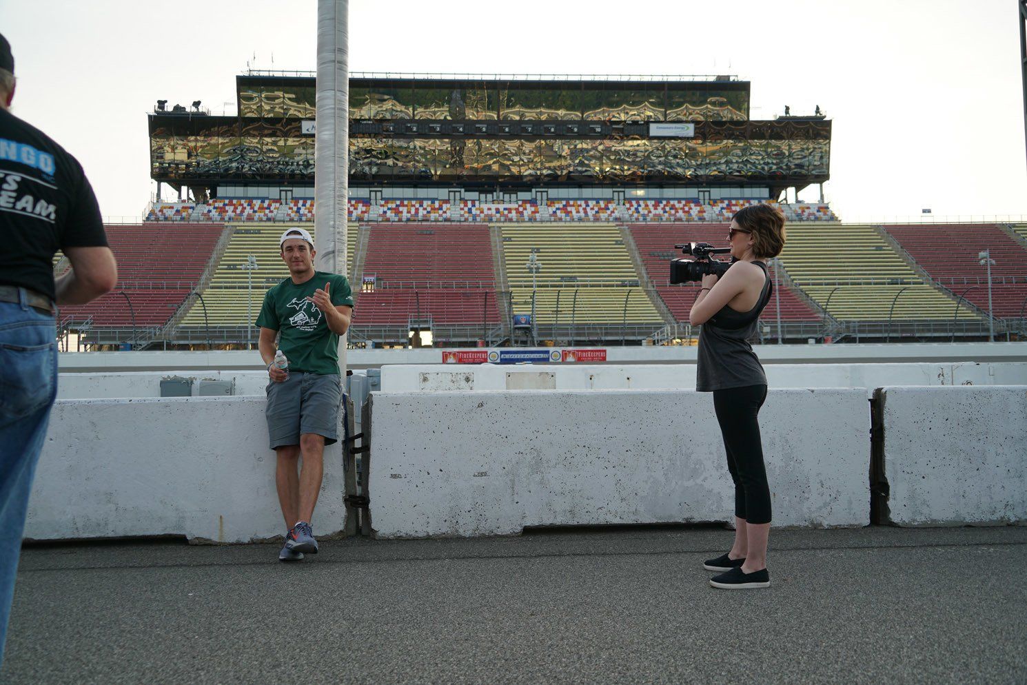 A woman is taking a picture of a man in front of a stadium