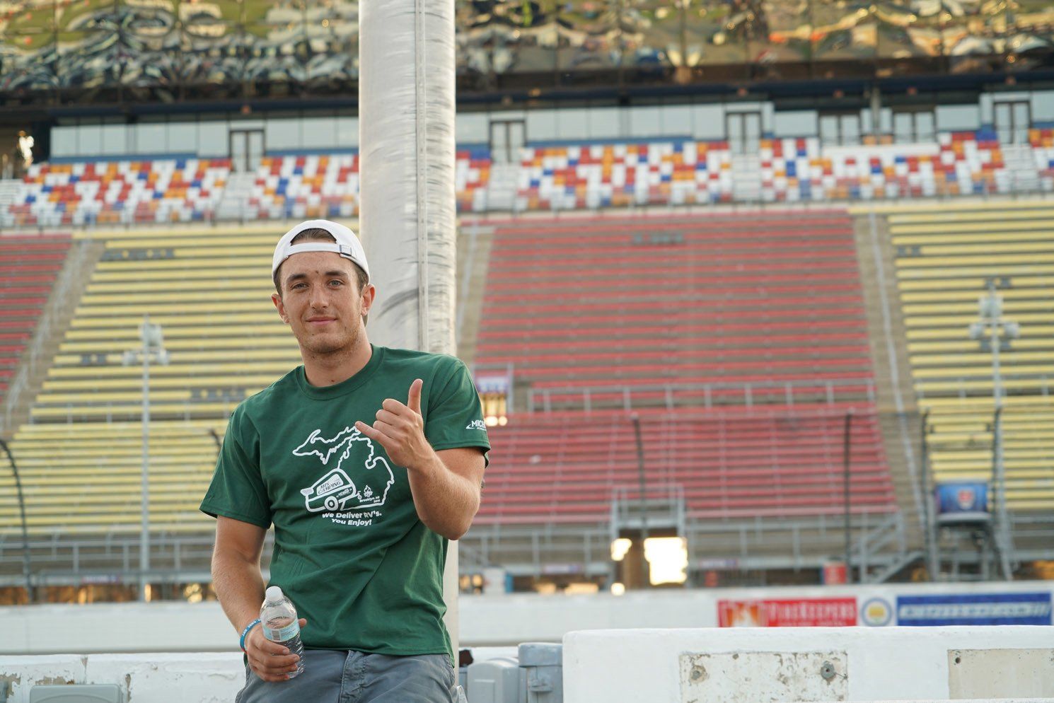 A man in a green shirt is giving a thumbs up in front of an empty stadium