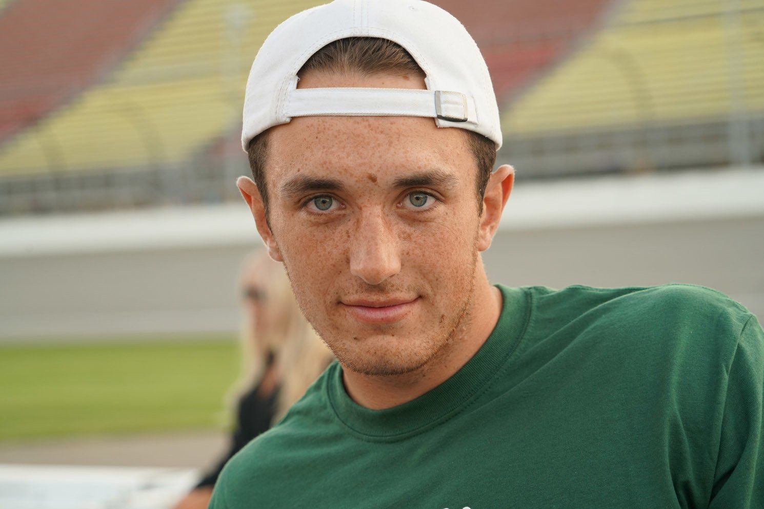 A young man wearing a green shirt and a white hat is looking at the camera.