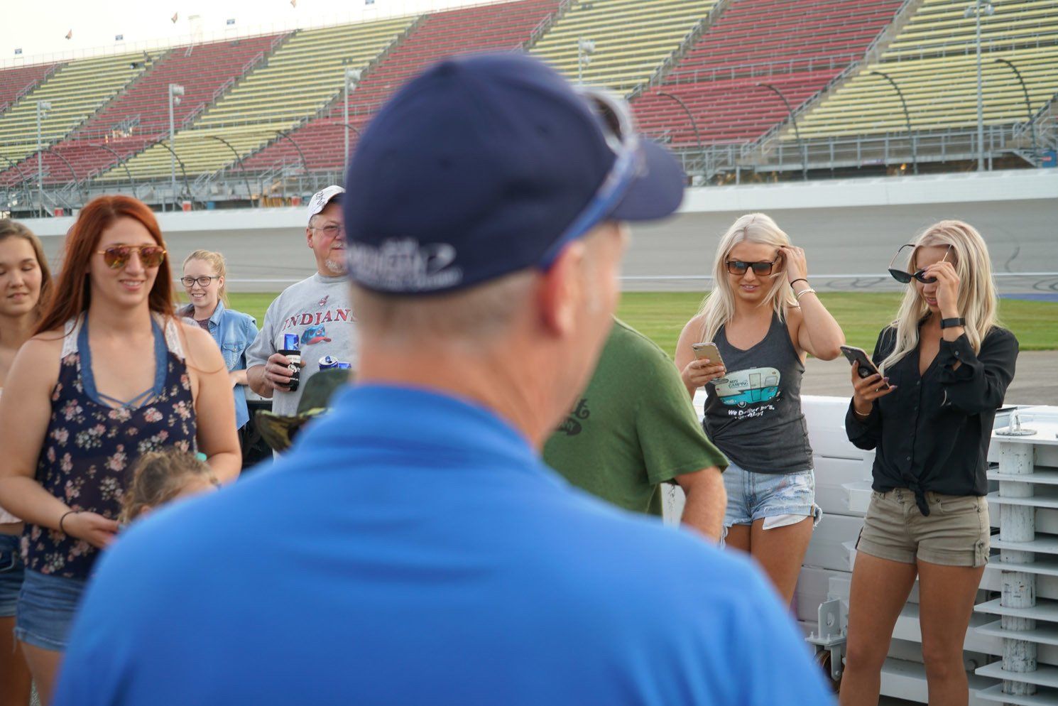 A man in a blue shirt is talking to a group of people on a race track.