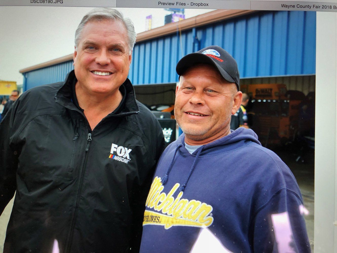 Two men are posing for a picture with one wearing a michigan sweatshirt