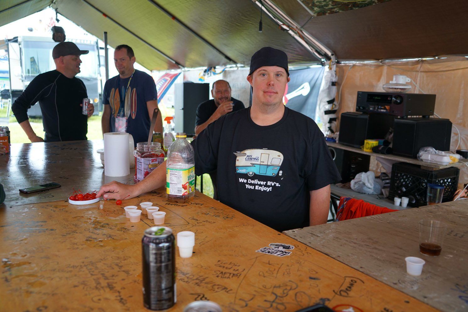 A man in a black shirt with a camper on it sits at a table