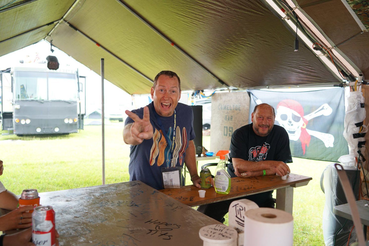 Two men sitting at a table under a tent with a pirate flag in the background