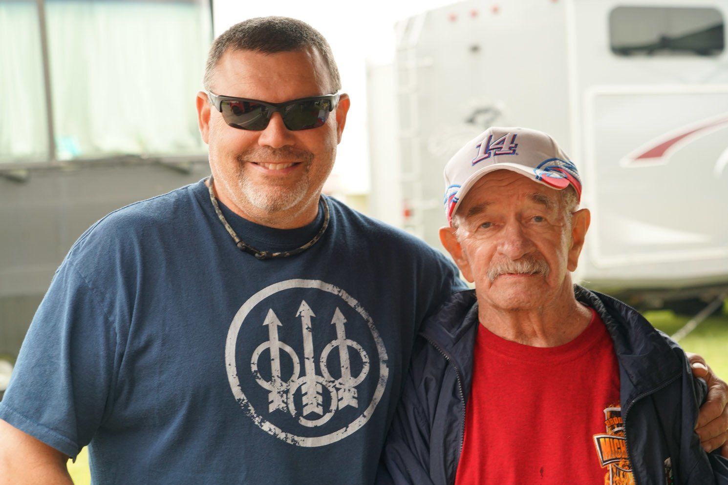 Two men are posing for a picture with one wearing a beretta shirt