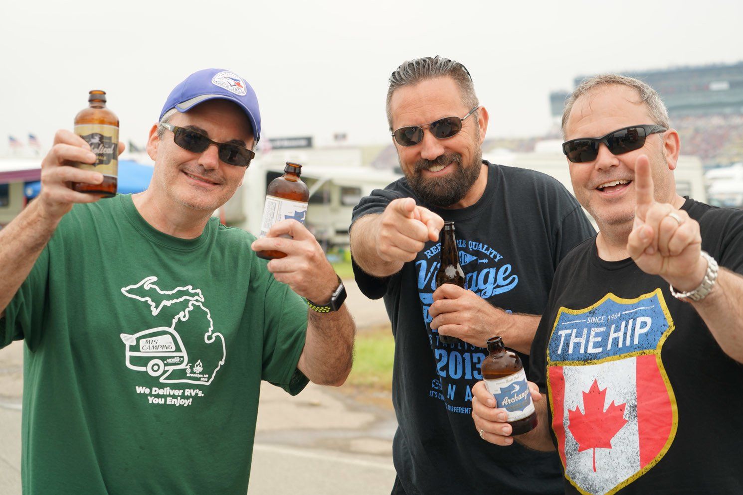 Three men are holding bottles of beer and one has a shirt that says the hip