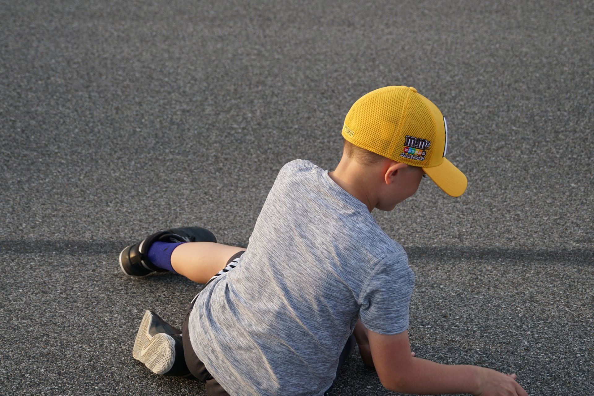A young boy wearing a yellow hat is kneeling on the ground.