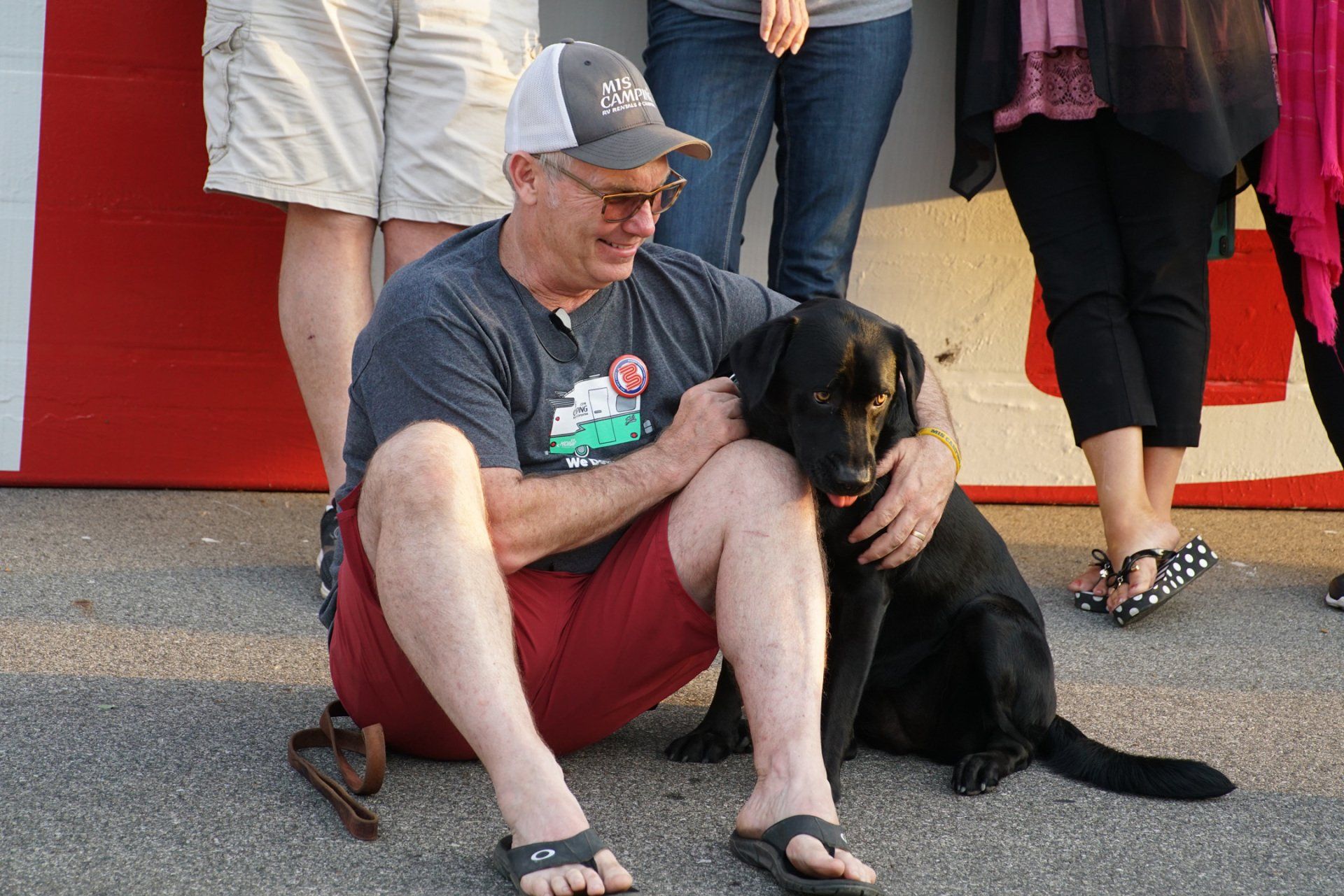 A man is kneeling down with a black dog on his lap.