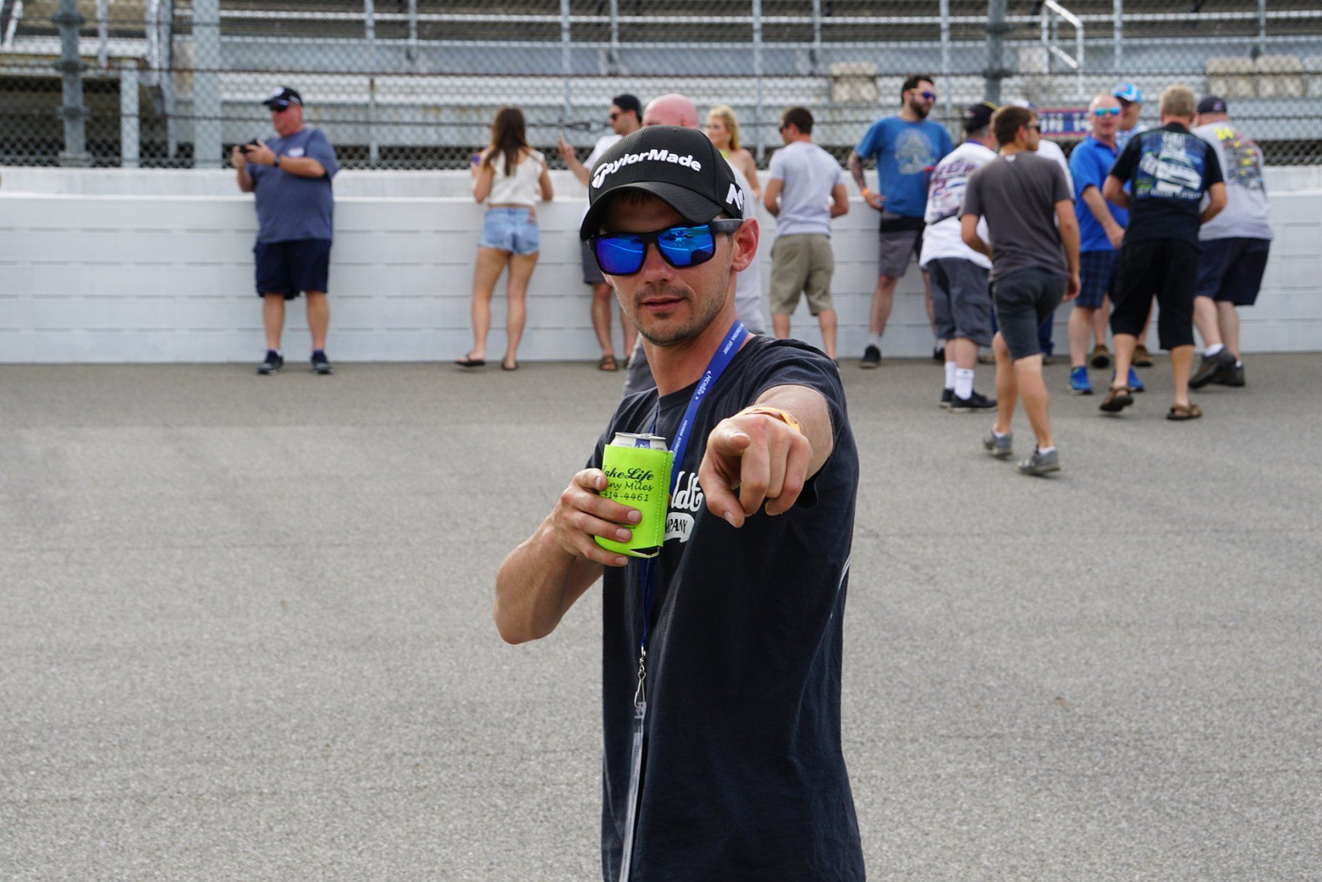 A man wearing sunglasses is pointing at the camera while holding a can of soda.