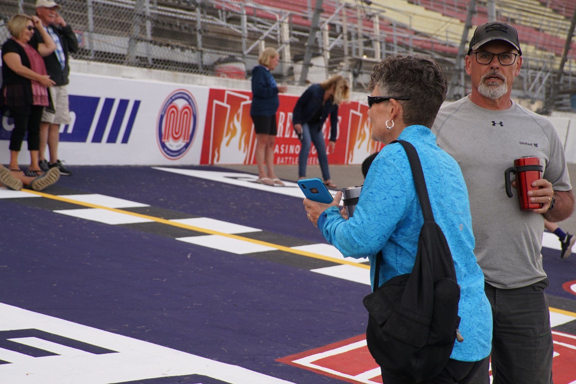 A man and a woman are standing on a race track talking to each other.