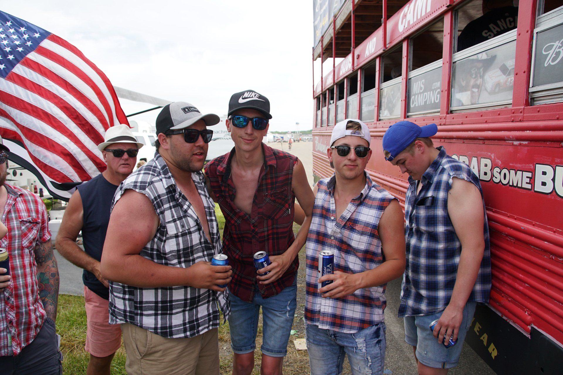 A group of men are standing in front of a red bus that says grab some beer on it.