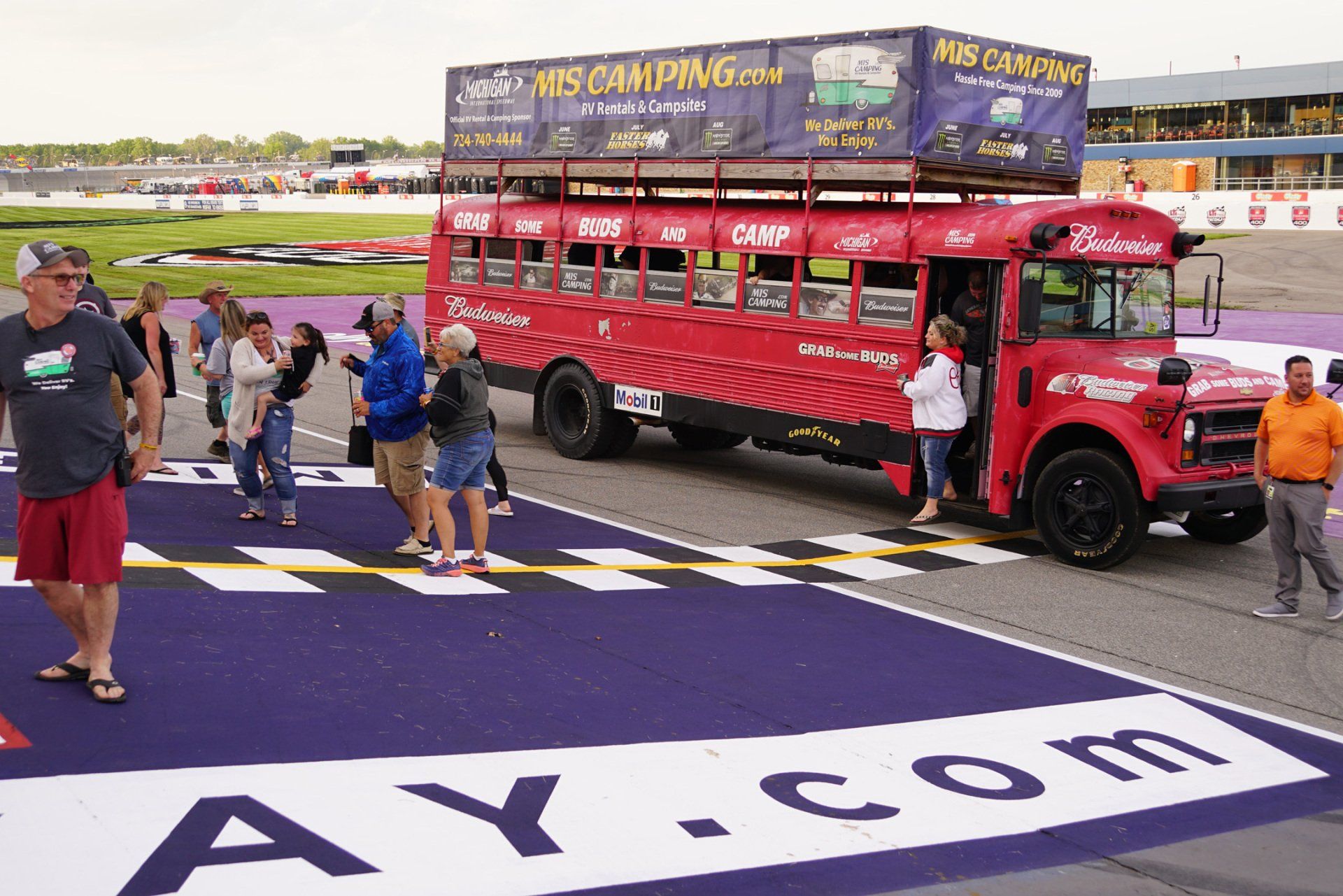 A group of people are walking towards a red bus on a race track
