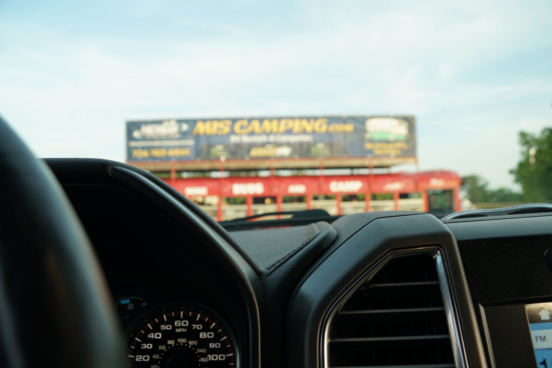 The inside of a car with a billboard in the background that says miscamping
