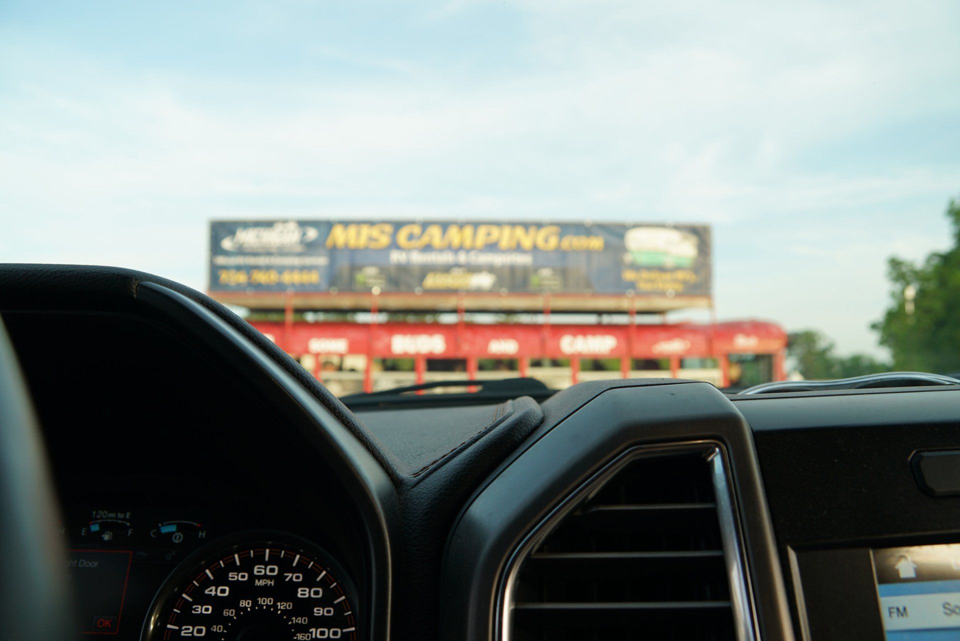 A dashboard of a car with a billboard in the background that says mps camping