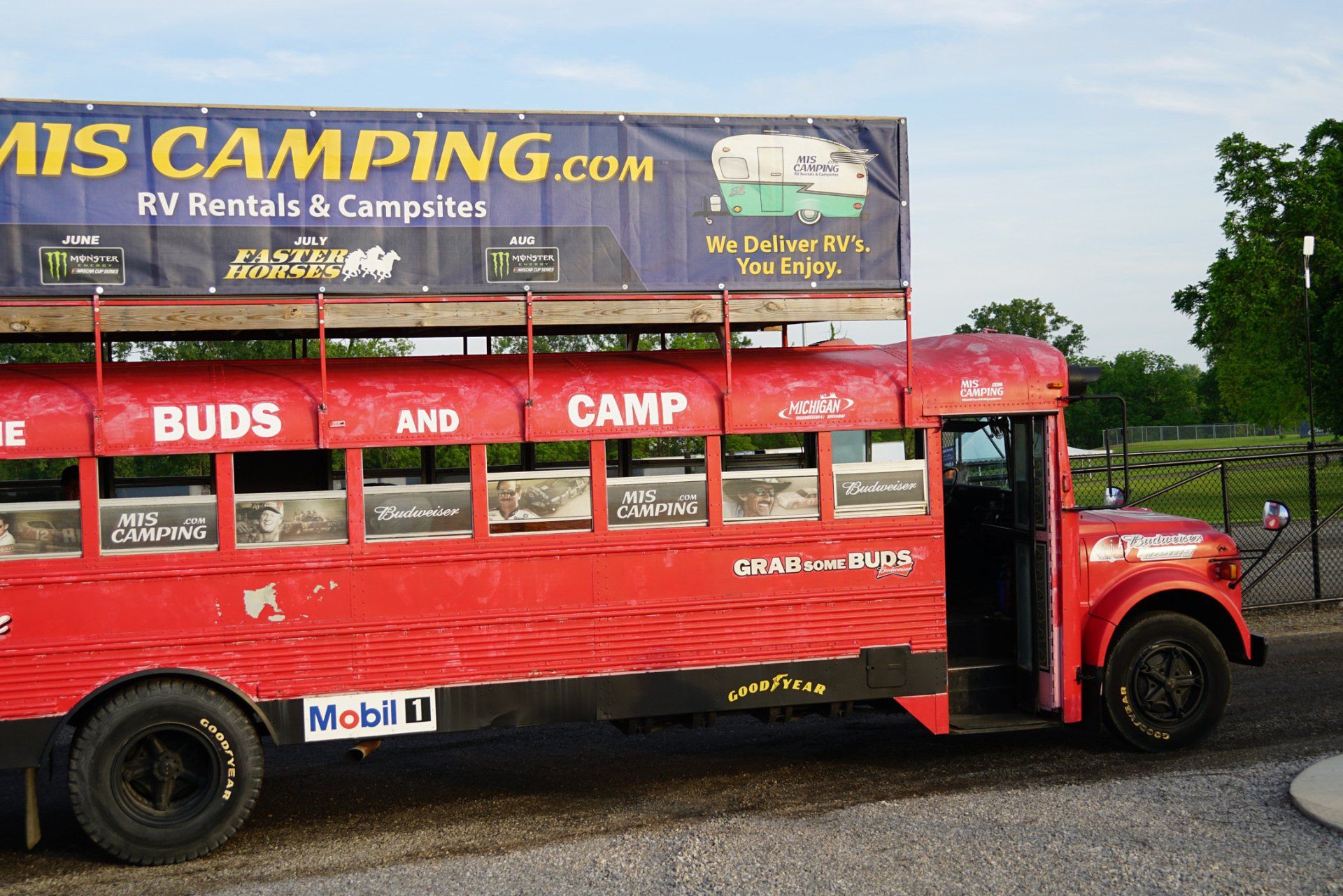 A red bus is parked in front of a sign that says miscamping.com