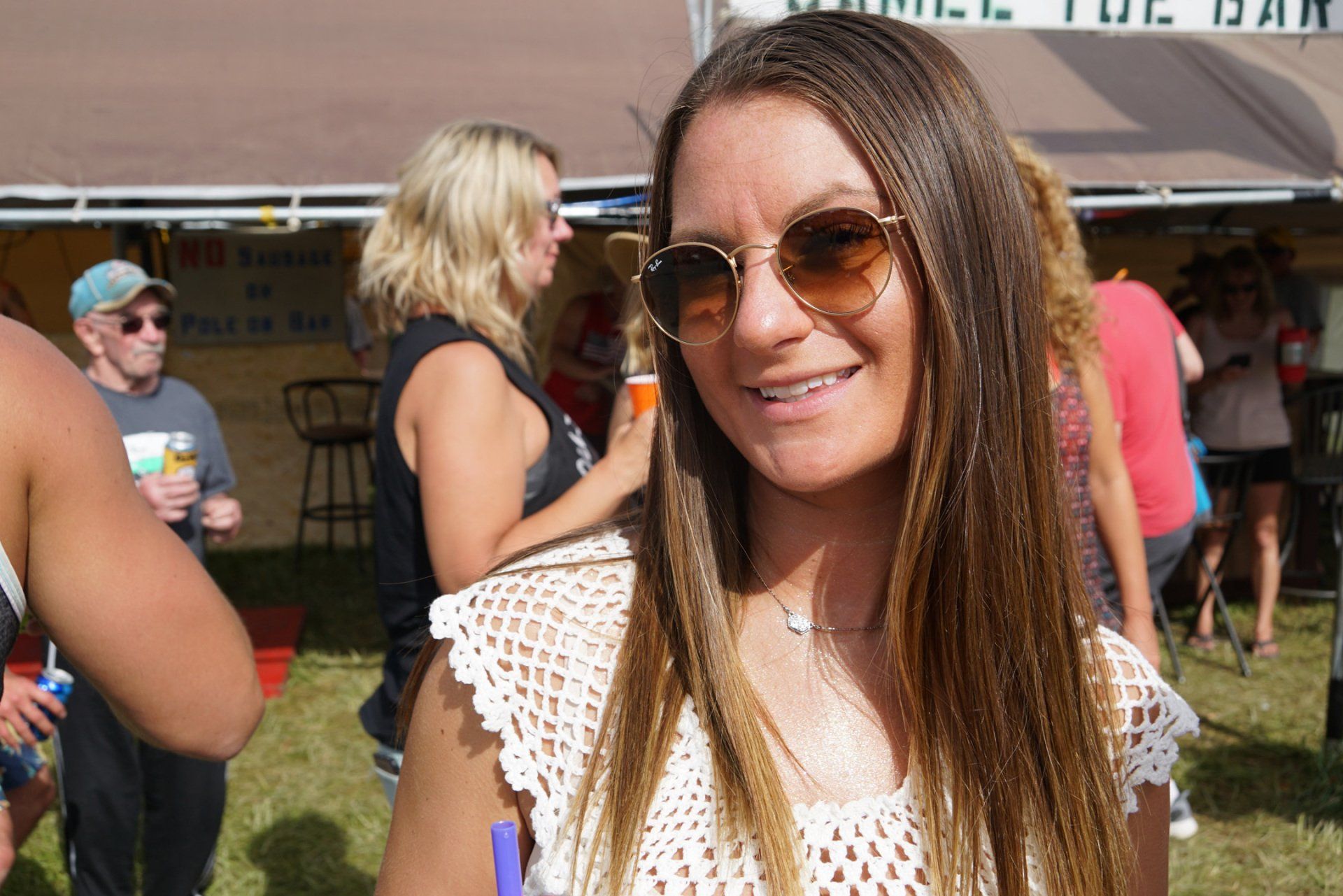 A woman wearing sunglasses is standing in front of a tent that says the bar