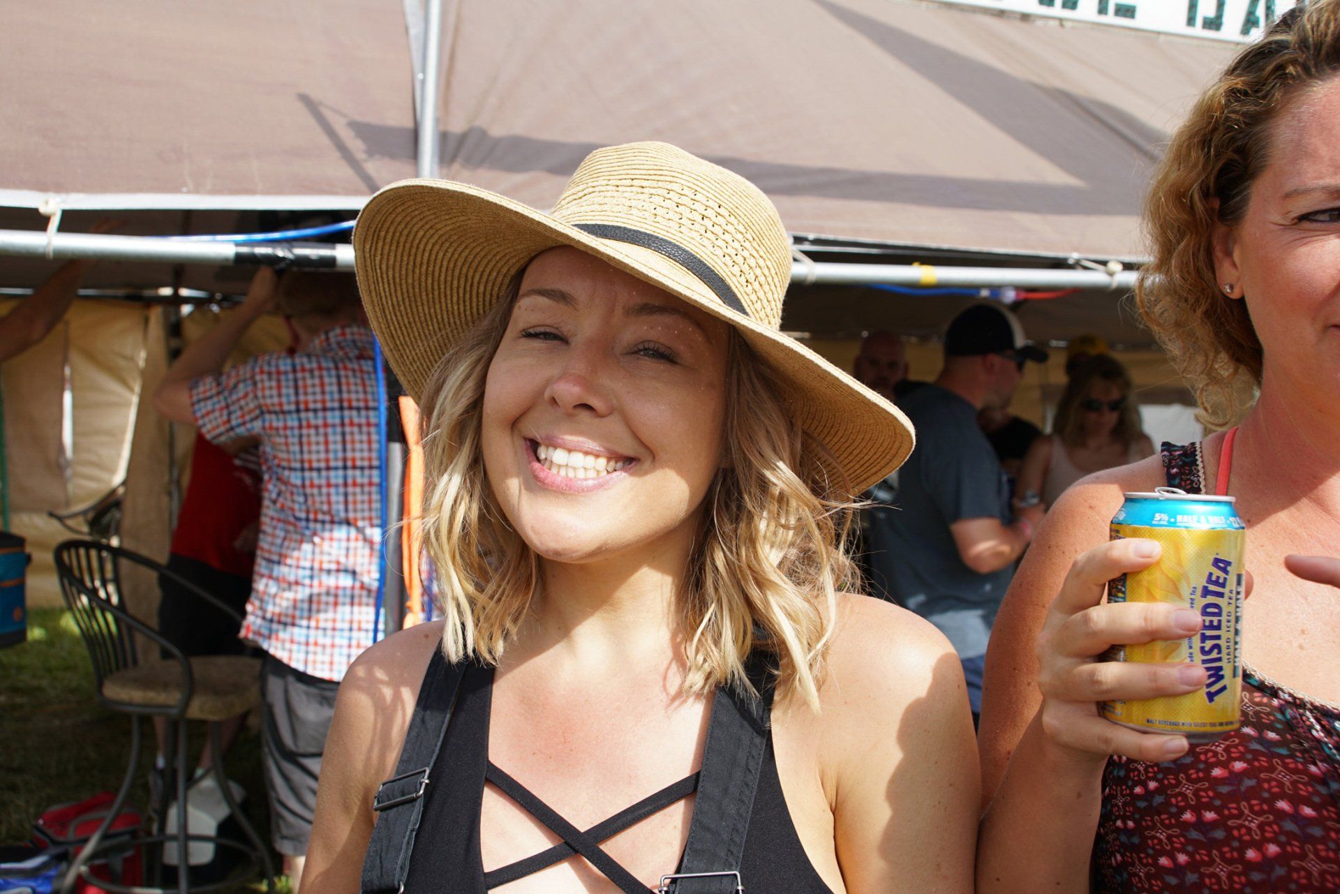 A woman wearing a straw hat is smiling while holding a can of beer.