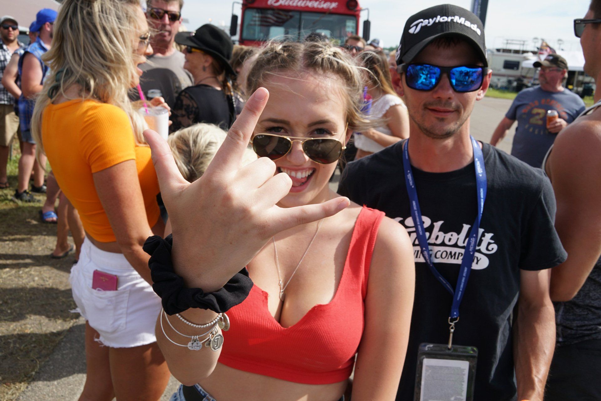 A woman in a red crop top is making a peace sign while standing next to a man in sunglasses.
