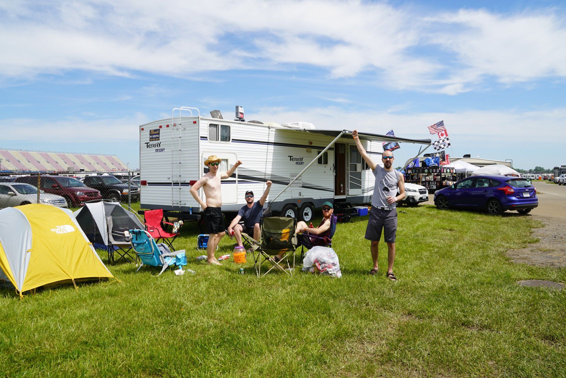 A group of people are sitting in front of a rv in a field.