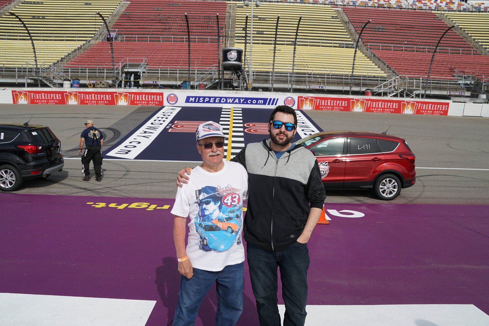 Two men are posing for a picture in front of a race track.