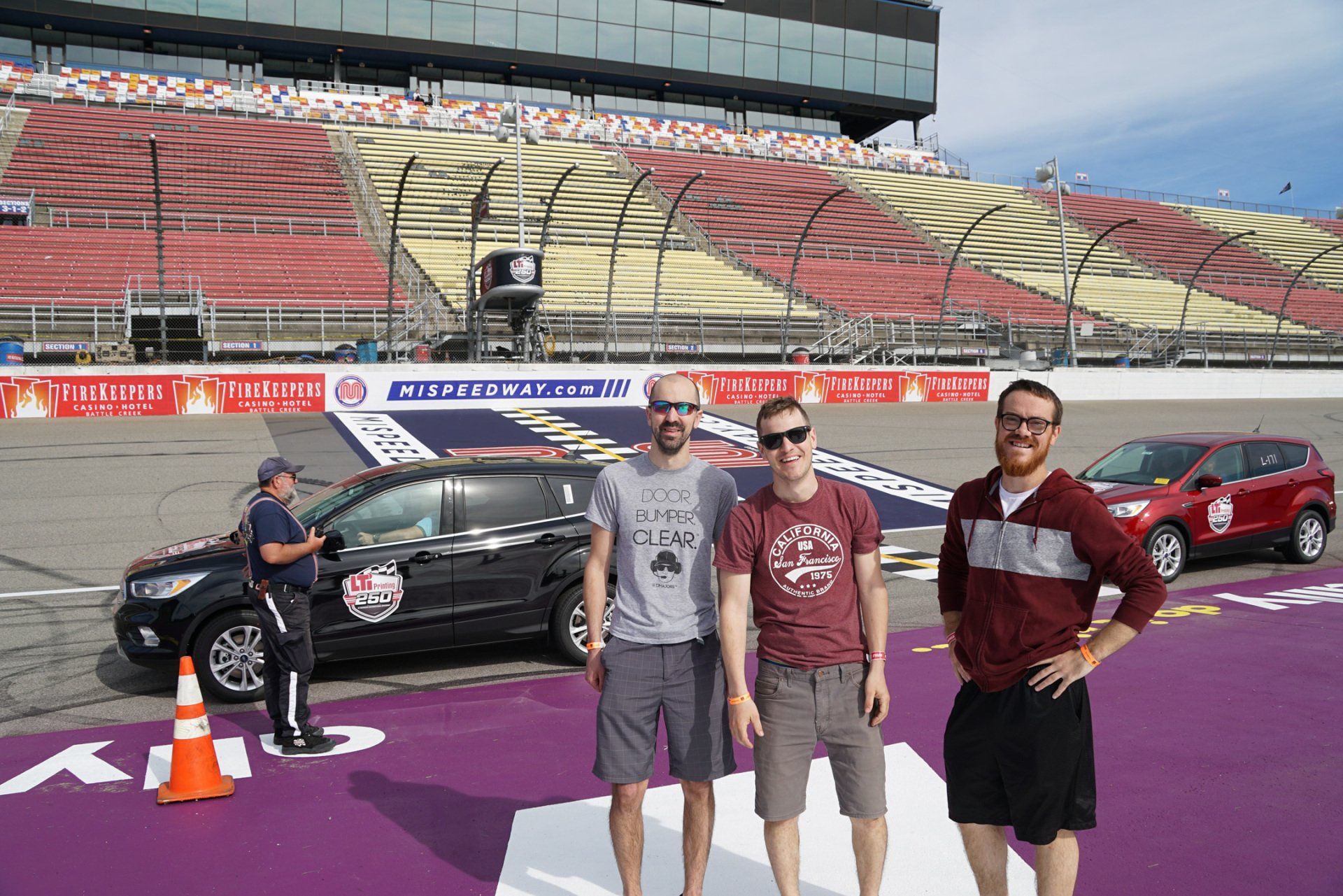 Three men are standing on a stage in front of a race track.