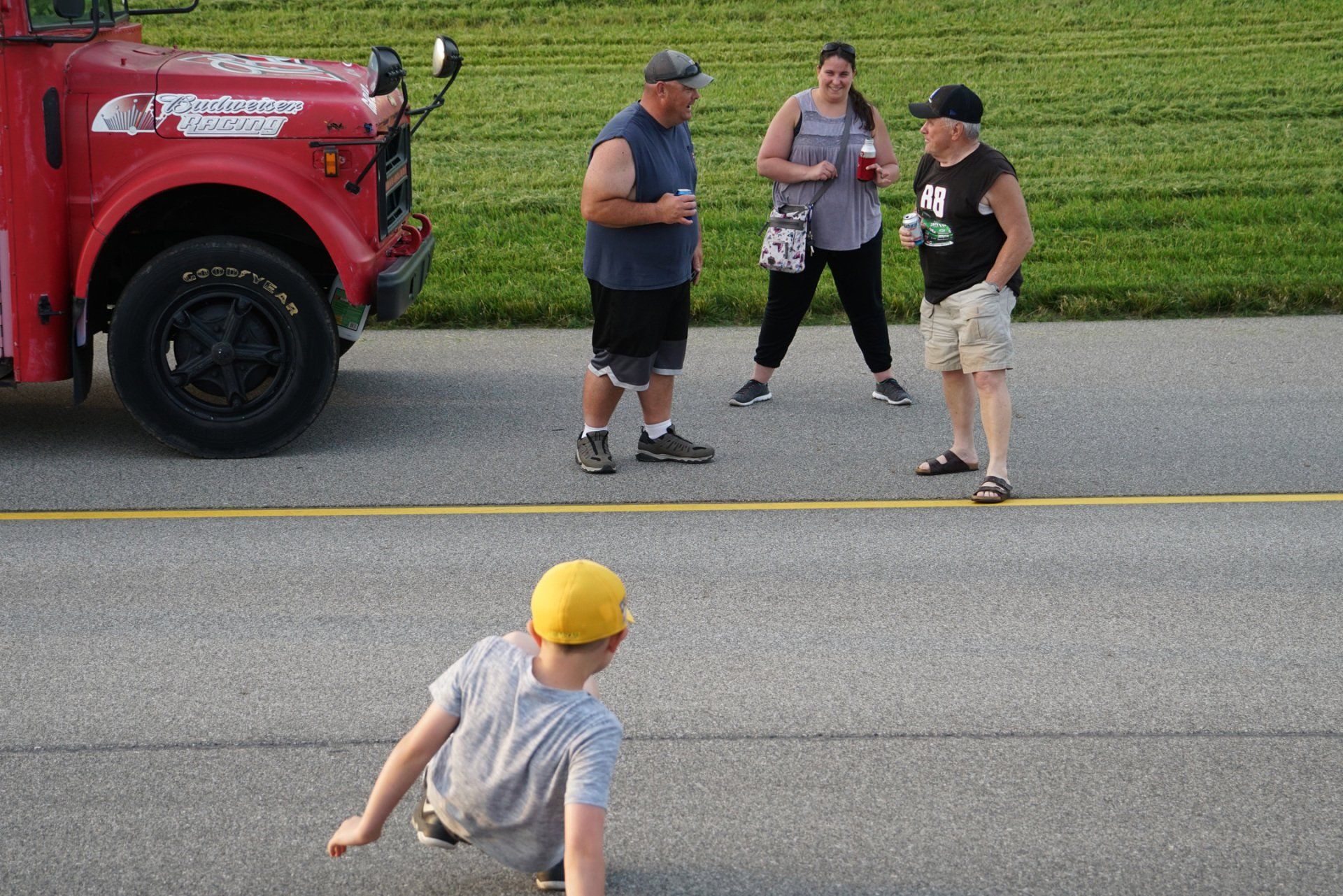 A group of people are standing on the side of the road next to a red truck.