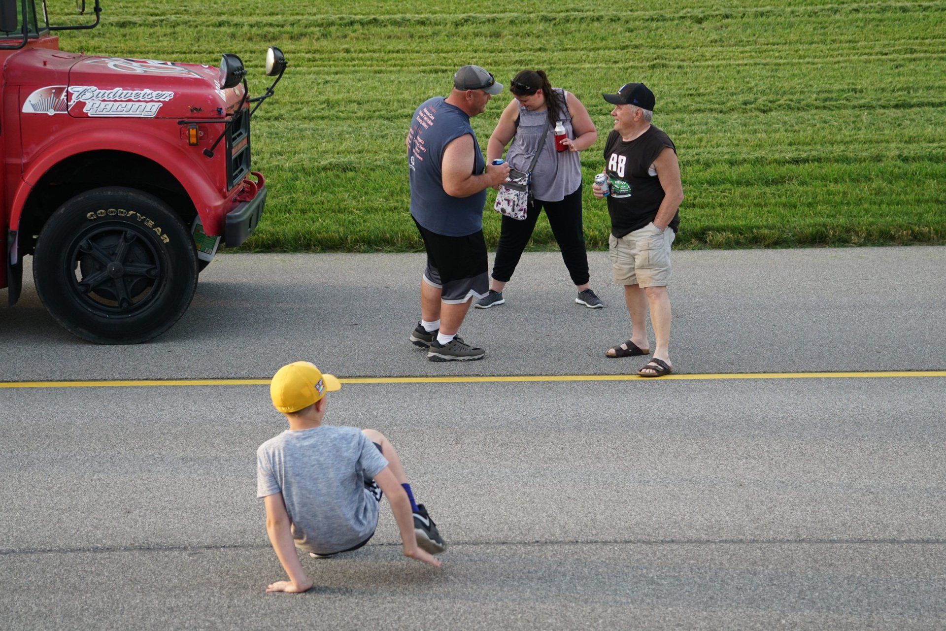 A group of people are standing on the side of a road in front of a truck that says budweiser on the front