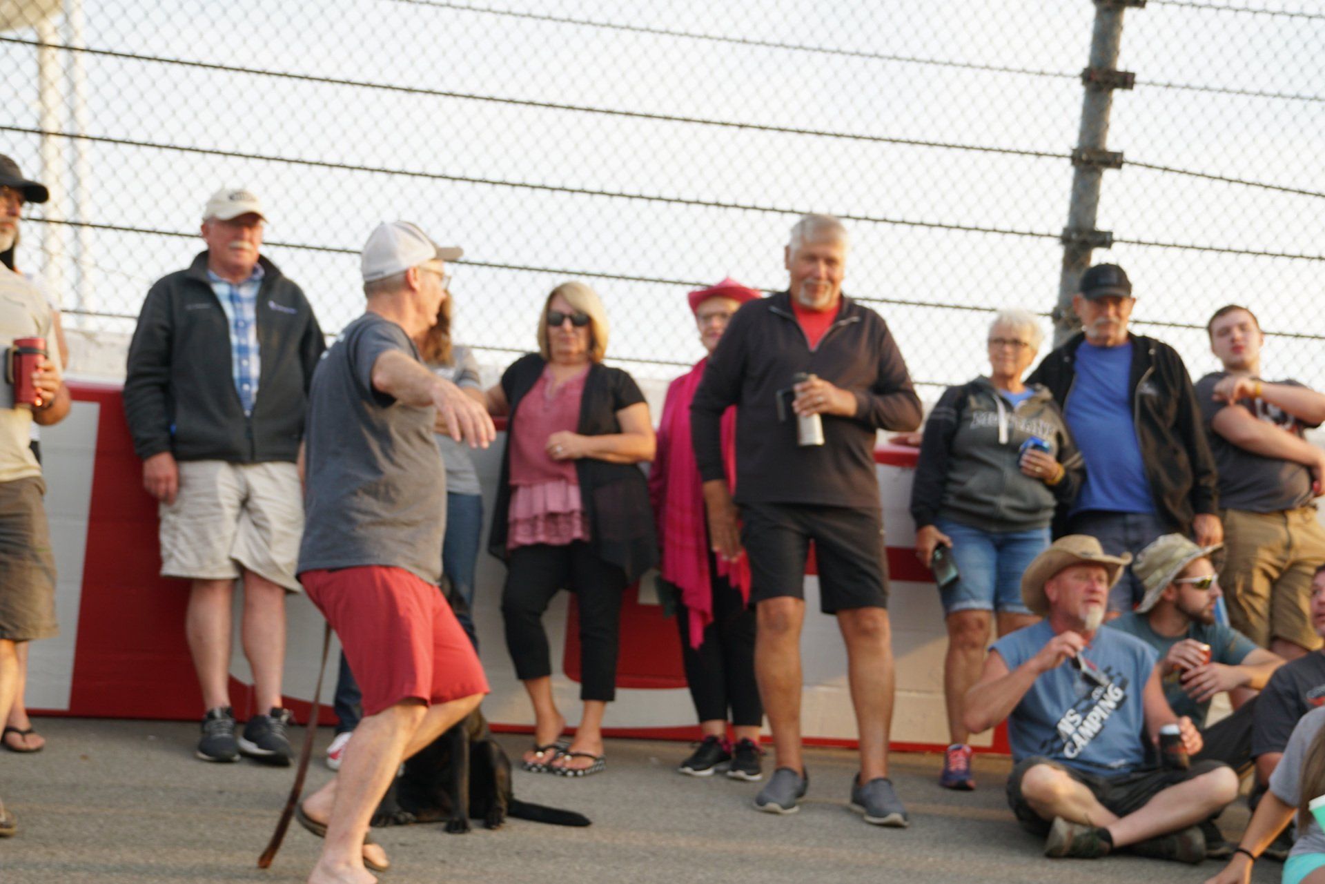 A group of people standing and sitting in front of a chain link fence