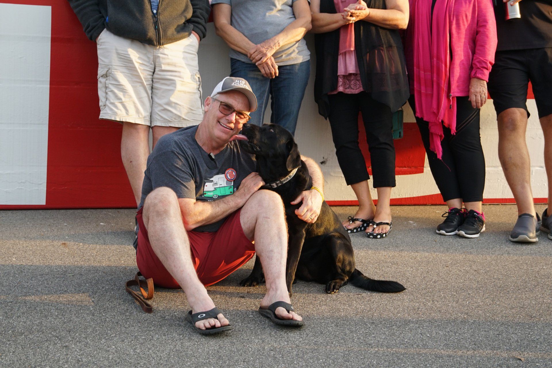 A man is kneeling down with a black dog in front of a group of people