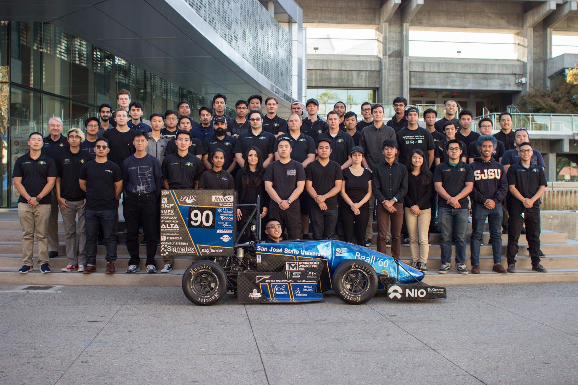 A group of people standing around a race car with the number 90 on it
