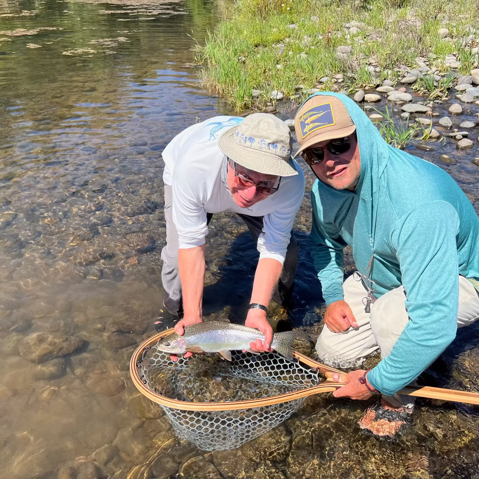 Two men, one holding a fish, in a shallow river, with a net.