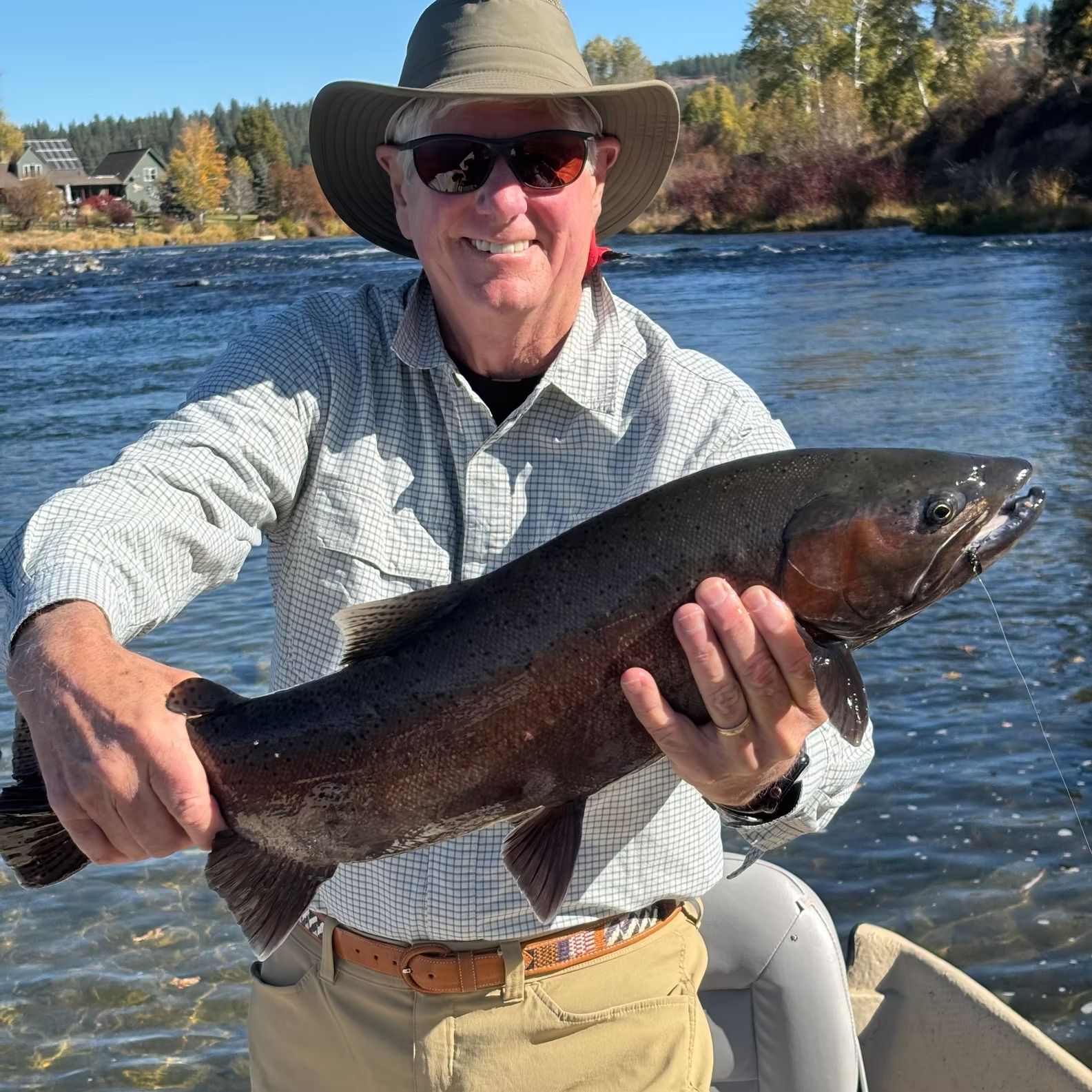 Man in hat holds a large dark fish in a river; smiling.