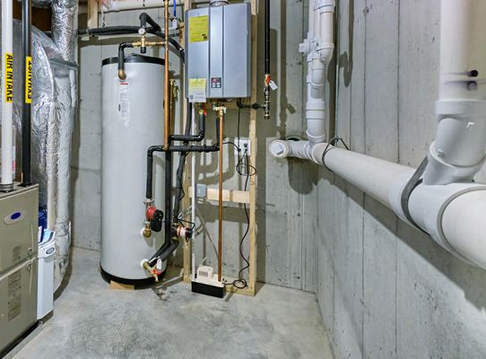 Water heater and plumbing in a basement utility room. Gray concrete walls and floor; pipes and equipment.