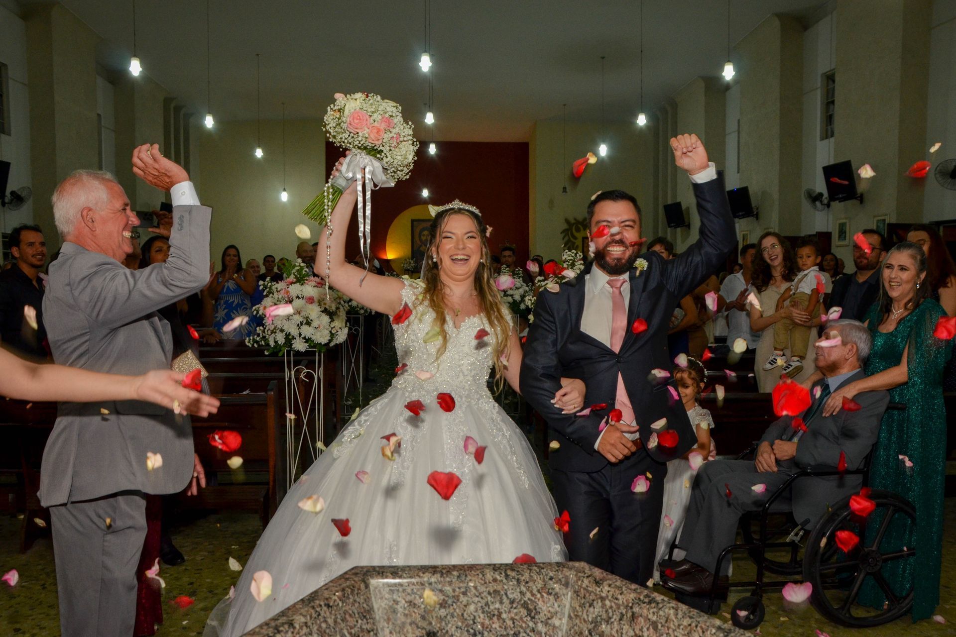 Recém-casados comemoram a saída do casamento com convidados jogando pétalas de rosas em uma igreja.