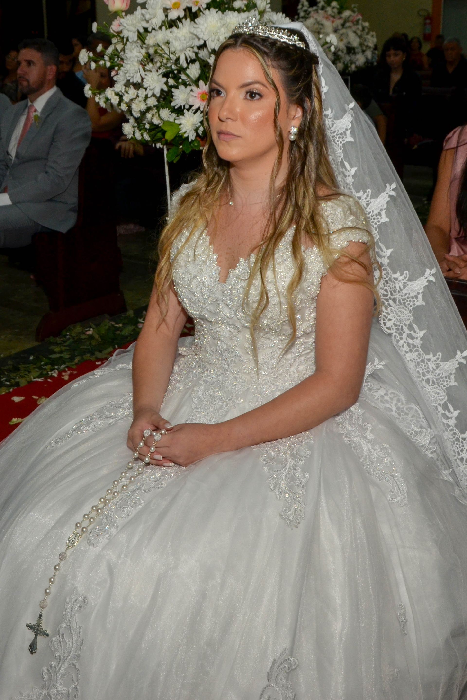 Noiva com vestido branco com renda e véu em cerimônia de casamento.